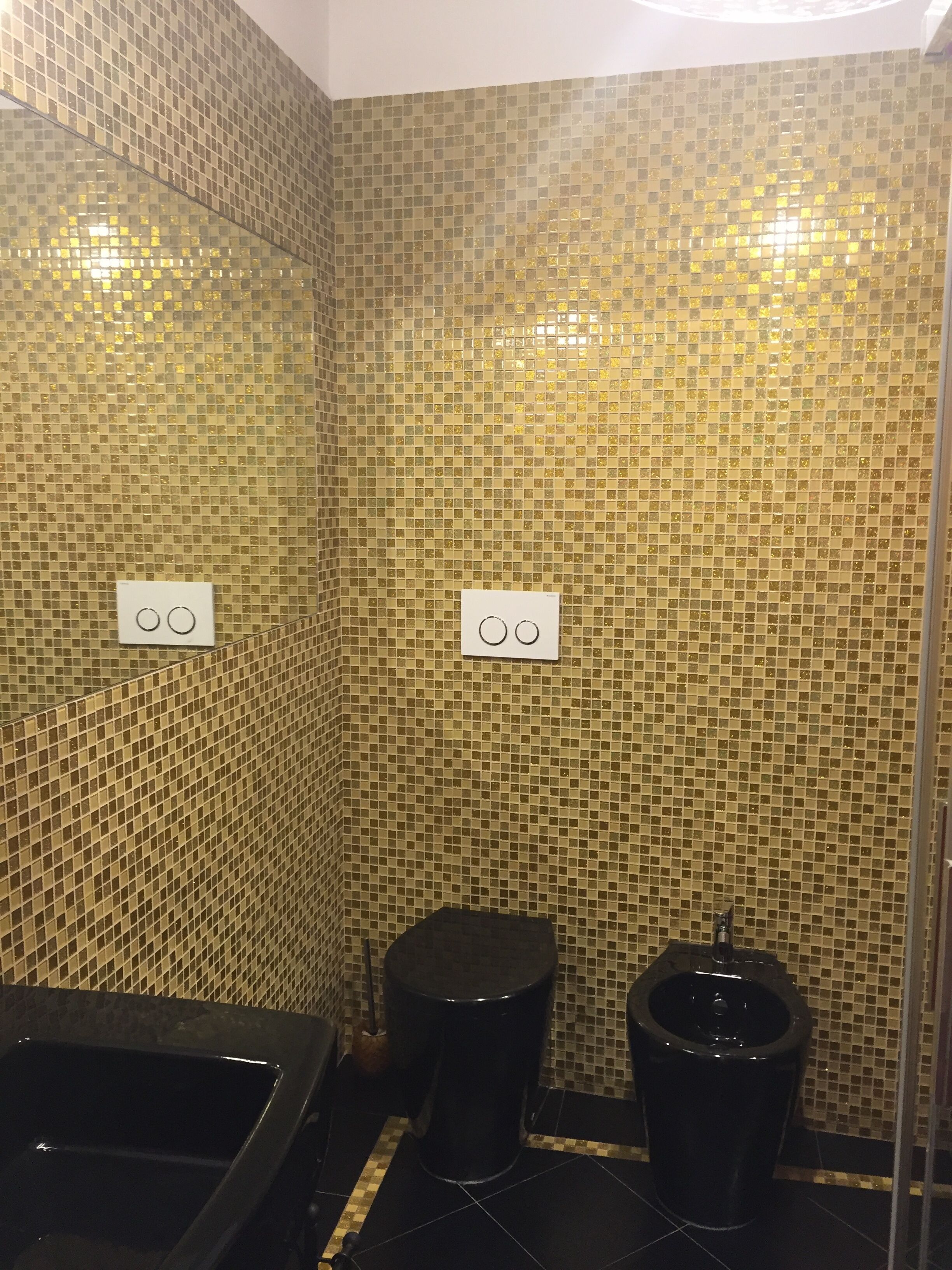 A bathroom with mosaic tile walls, two toilets, and a bathtub.