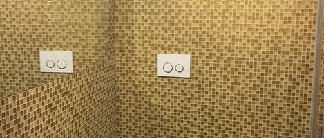 A bathroom with mosaic tile walls, two toilets, and a bathtub.