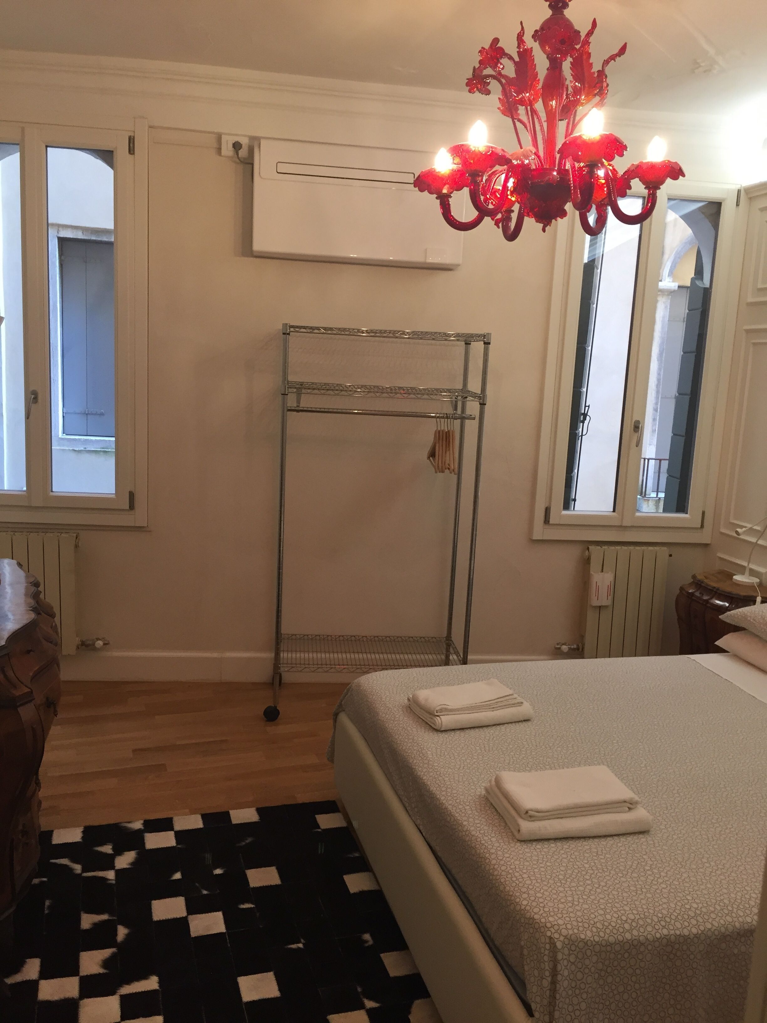 A bedroom with a bed, a metal drying rack, a chandelier, and a window.