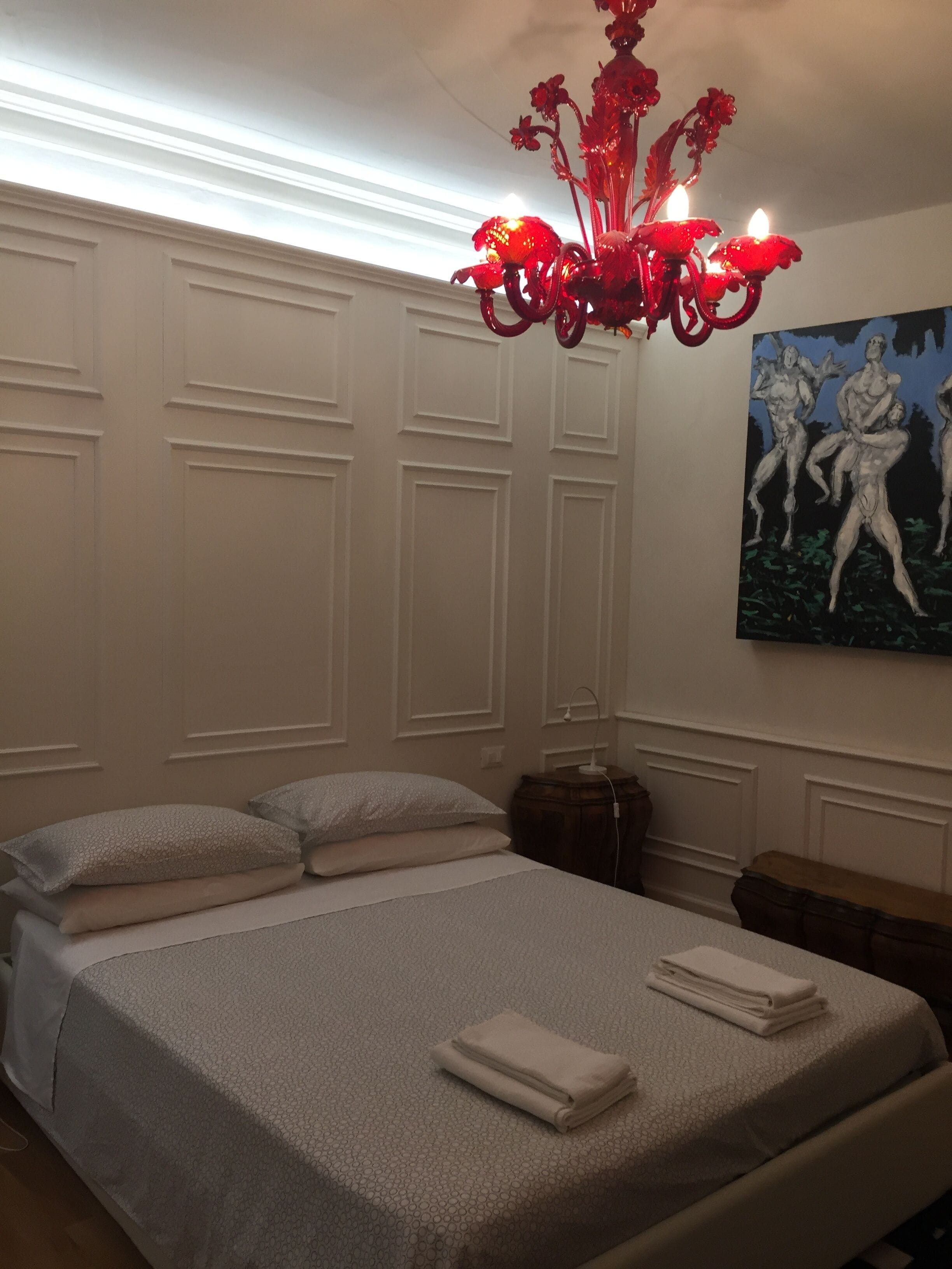 A bedroom with a bed, pillows, a bedside table, a lamp, and a painting on the wall.