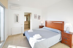 A hotel room with a large bed, wooden headboard, two bedside tables with lamps, a radiator, a mirror, and a door leading to a bathroom.