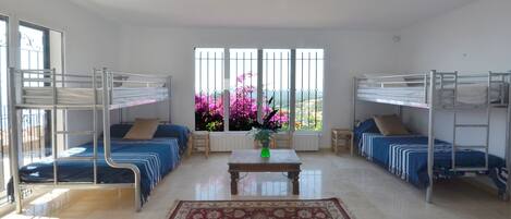 A room with bunk beds, a central table, and a large window with pink flowers.