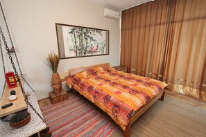 A bedroom with a bed, a hanging chair, a small table with a lantern, and a wall-mounted air conditioner.