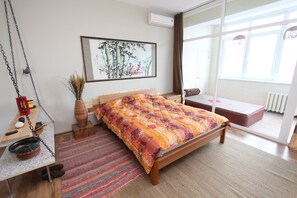 A bedroom with a bed, a desk with a chair, a window, and a radiator.