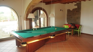 A pool table in a room with a rustic ceiling, a stone wall, and a view through an arched doorway. - Villa on the Tuscan hills near Florence (Castelfranco Piandiscò)