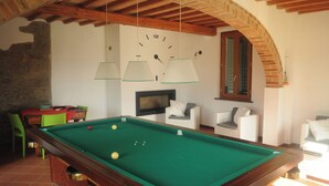 A billiards table with balls, a fireplace, and two white armchairs in a room with exposed wooden beams and a stone wall. - Villa on the Tuscan hills near Florence (Castelfranco Piandiscò)