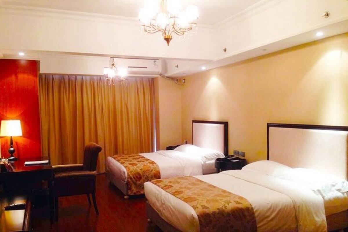 A hotel room with two beds, a desk, a chair, a lamp, and a chandelier.