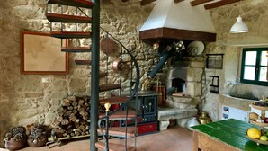A rustic kitchen with a stone wall, a wooden staircase, a wood-burning stove, and a tiled floor. - UNA RARA AVIS - solar house with sea views (Porto do Son (A Coruña))