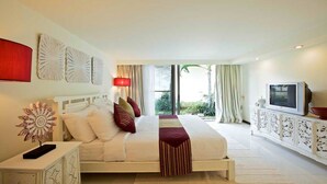 A hotel room with a bed, a TV, a decorative wall piece, and a view of greenery outside. - Baan Ban Buri (Koh Samui)