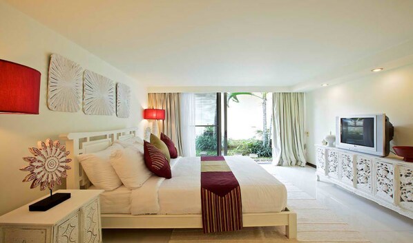 A hotel room with a bed, a TV, a decorative wall piece, and a view of greenery outside. - Baan Ban Buri (Koh Samui)