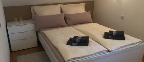 A neatly made bed with two pillows, a bedside table with glasses, and a wall-mounted light.