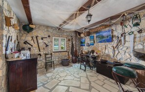 Une pièce rustique aux murs de pierre, dotée d’un sol en pierre, de meubles en bois et de divers outils et objets de décoration.