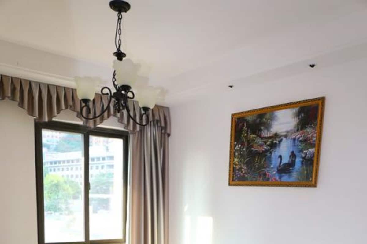Habitación de hotel con cama, mesita de noche, un cuadro, ventana con cortinas y un candelabro.