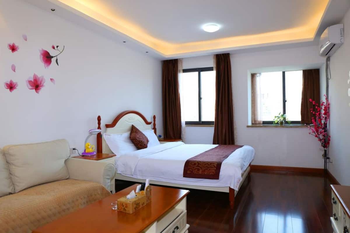 Una habitación de hotel con una cama, una mesita de noche con lámpara, un sofá, una ventana con cortinas y un aire acondicionado instalado en la pared.