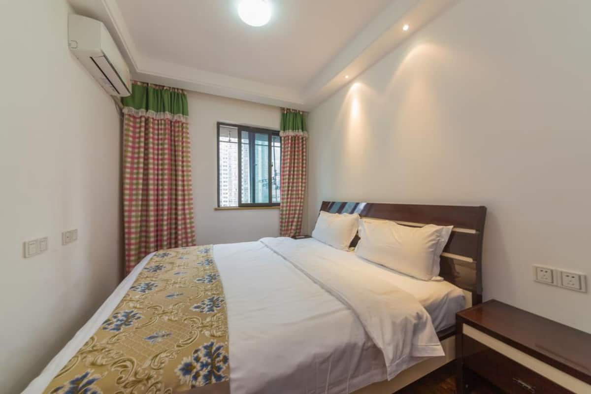 Un dormitorio con cama, mesita de noche, aire acondicionado y ventana con cortinas.