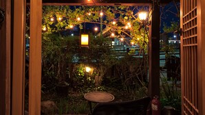Un espace extérieur aménagé en terrasse, avec des guirlandes lumineuses, une table et une chaise.