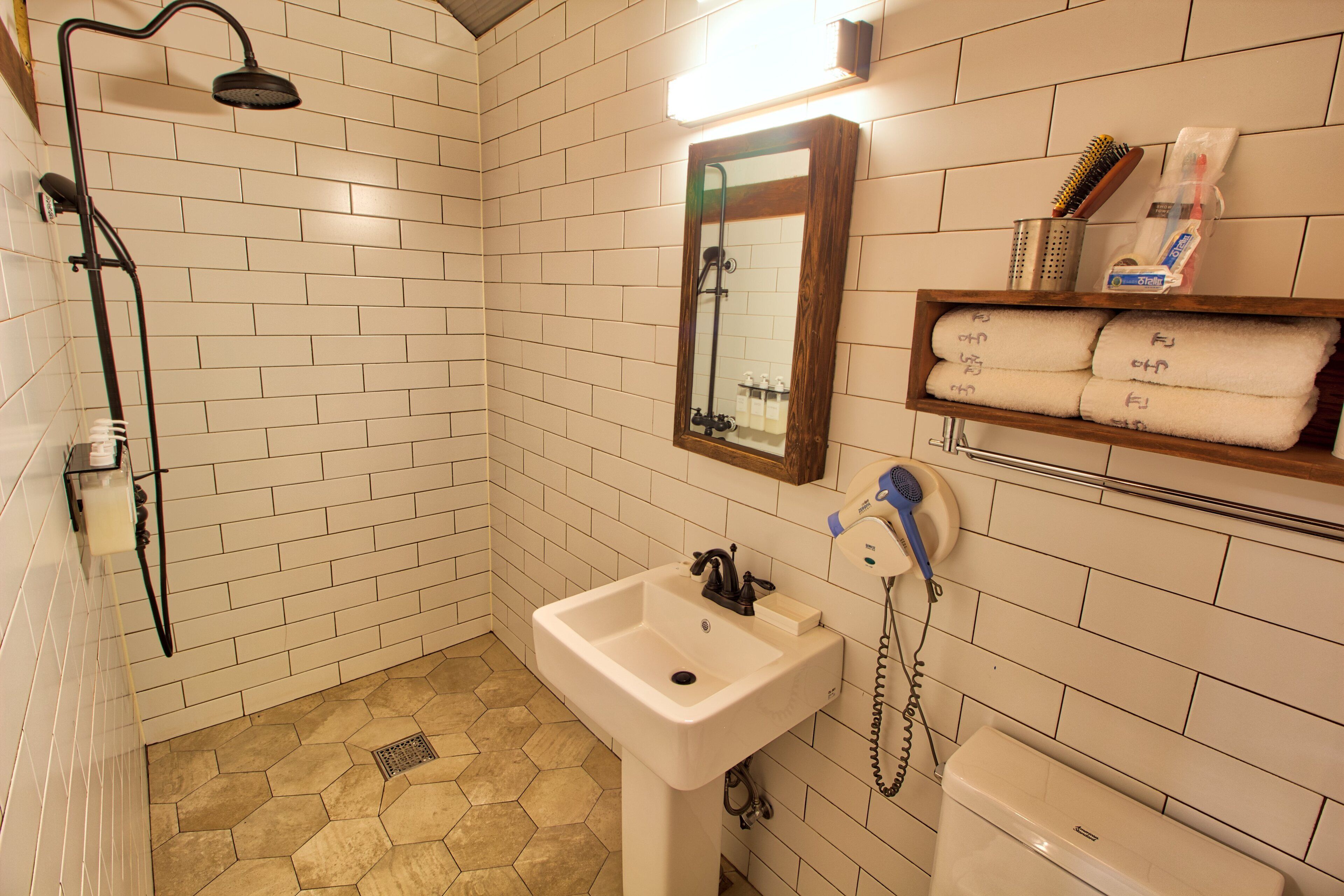 Un baño con lavamanos blanco, ducha, espejo y estante con toallas.