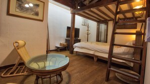 Une pièce avec un lit superposé, une table en verre, une chaise en osier, un tableau encadré accroché au mur et un téléviseur posé sur un meuble.