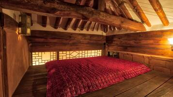 A wooden cabin with a sloped ceiling, a bed with a red blanket, and a window with a geometric pattern.