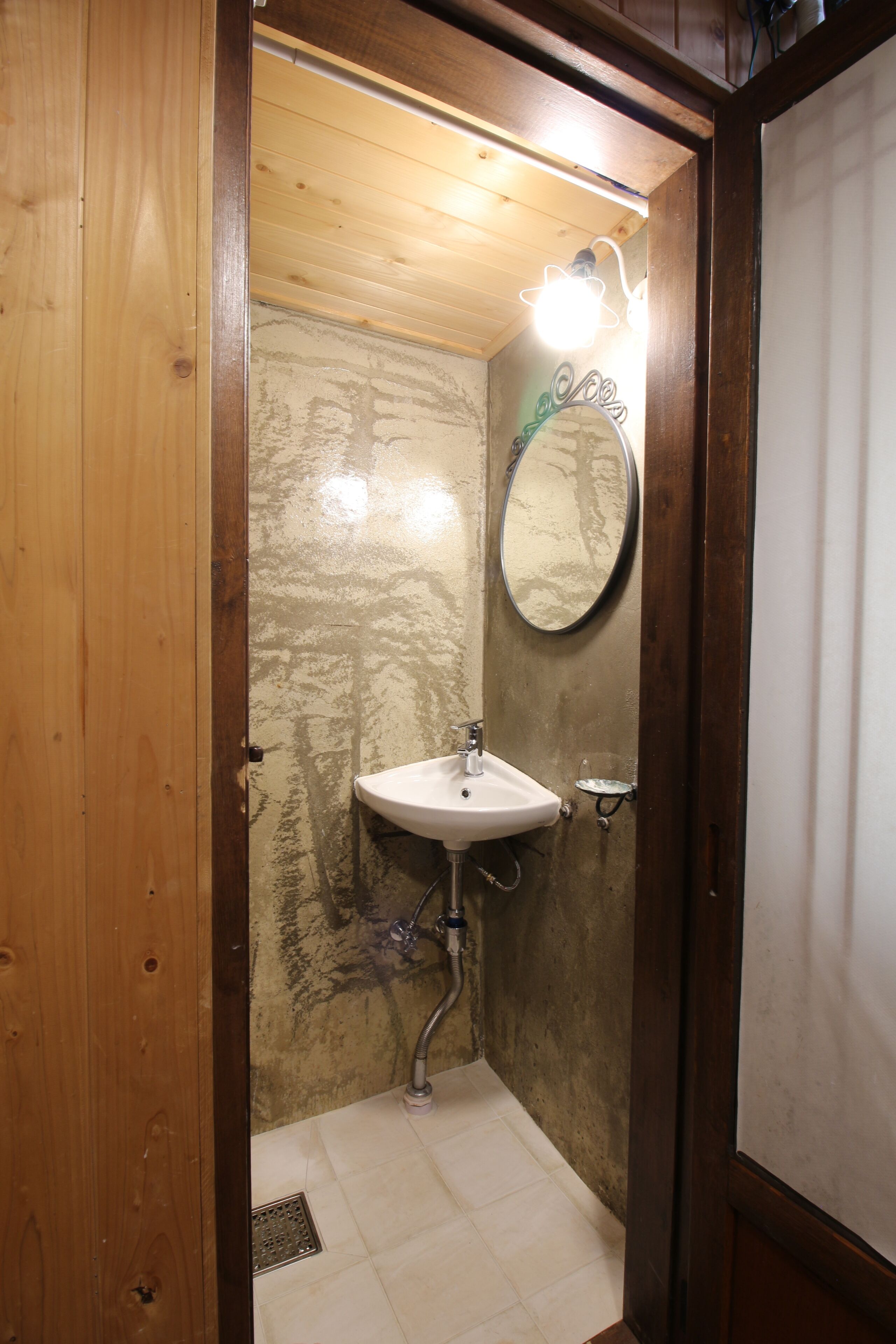 A small bathroom with a wooden door, a white sink, a mirror, and a light fixture.