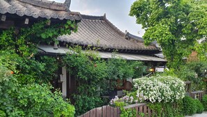Un bâtiment traditionnel avec un toit en tuiles, entouré d’une végétation luxuriante et d’une clôture en bois.