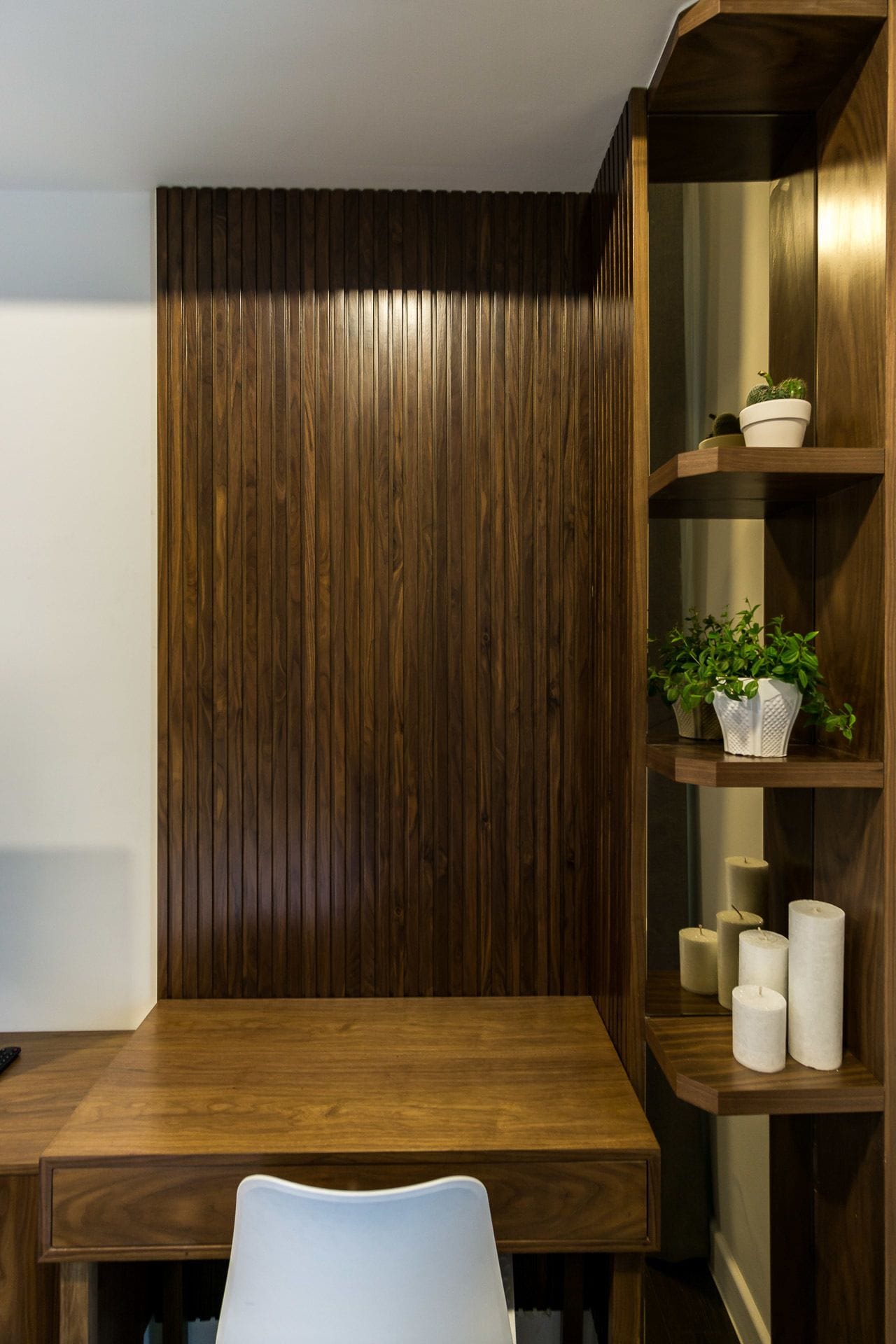 A wooden dining table with a white chair in front, a wooden cabinet with shelves, and a wall with vertical wooden slats.