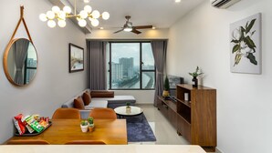 A modern living room with a dining area, large windows with curtains, a ceiling fan, and a view of the cityscape. - Rivergate Apartment - MM Home (Ho Chi Minh City)
