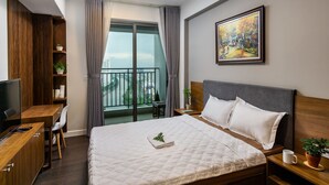 A modern hotel room with a large bed, a desk, a TV, and a balcony with a city view. - Rivergate Apartment - MM Home (Ho Chi Minh City)
