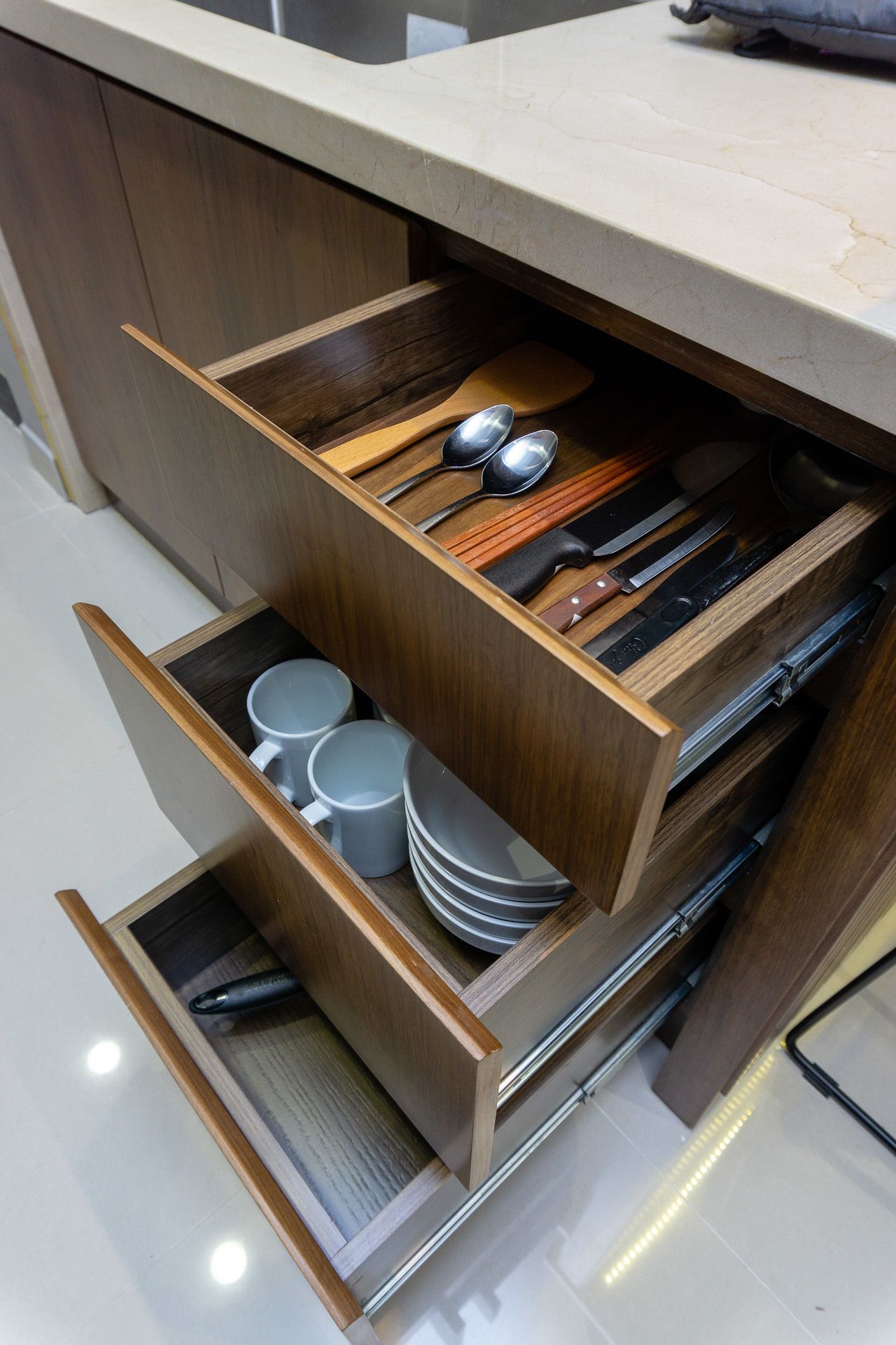 Une cuisine dotée de meubles de rangement en bois et d’un meuble à tiroirs intégré contenant des ustensiles, des assiettes et des tasses.