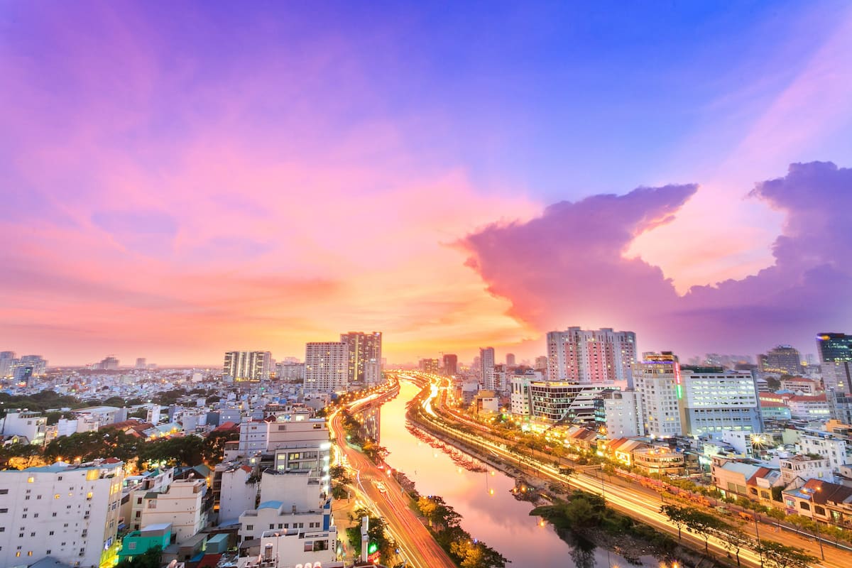 Paisagem urbana ao pôr do sol com um rio serpenteando entre edifícios altos.