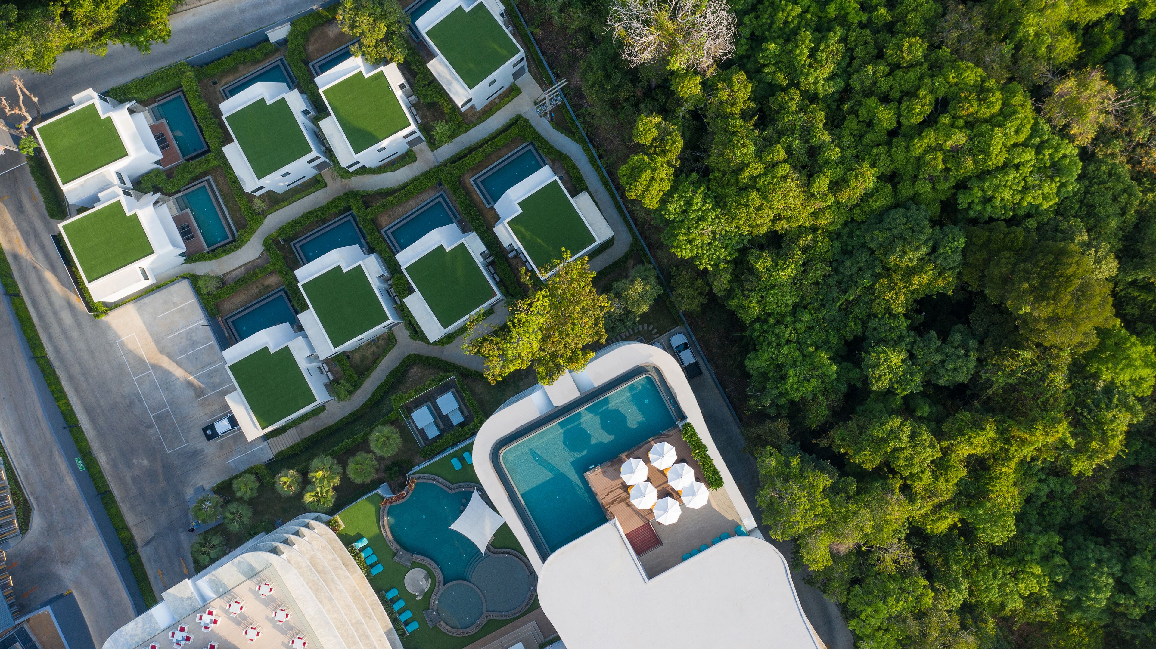 An aerial view of a resort with multiple swimming pools, lush greenery, and a large central pool with sun loungers.