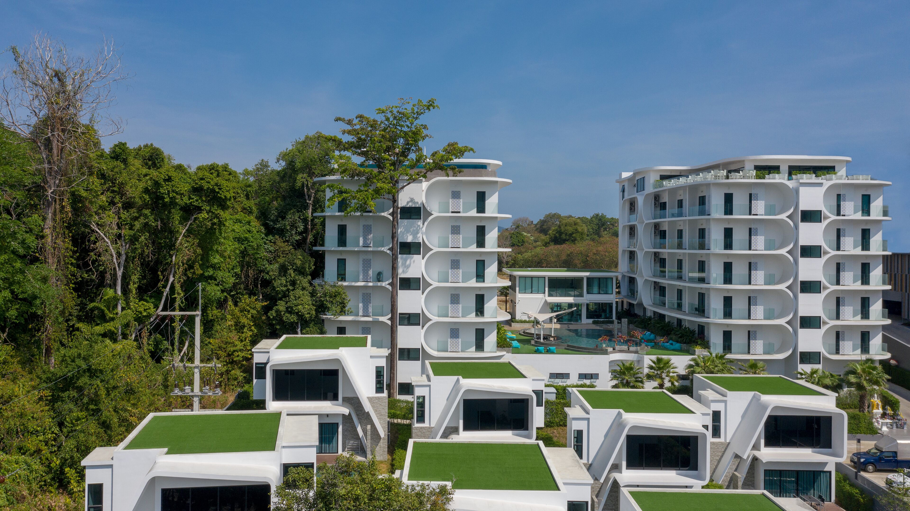 Un hotel moderno con varias edificaciones blancas, balcones y techos verdes.