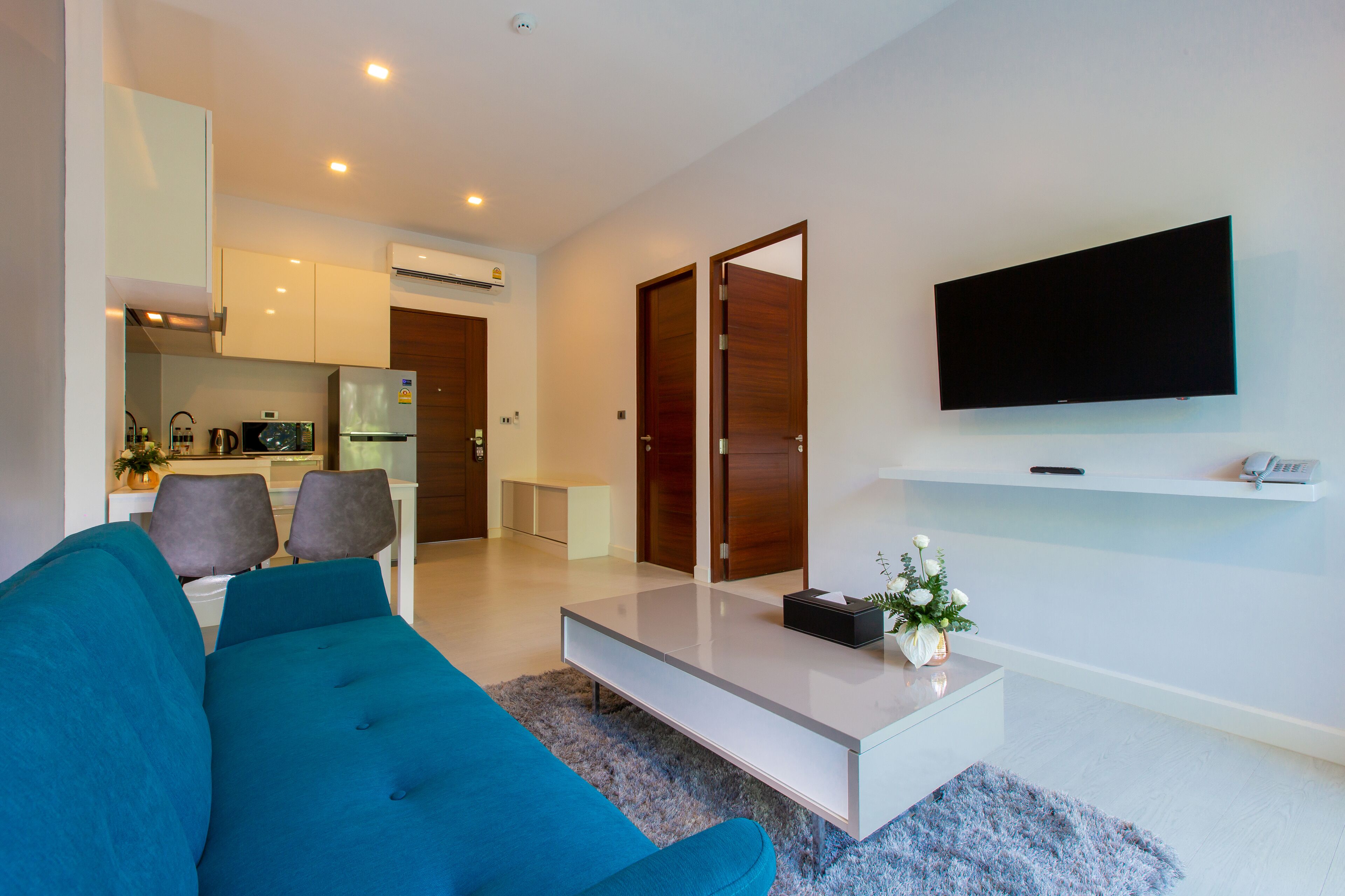 A modern living room with a blue sofa, a coffee table, and a flat-screen TV mounted on the wall.