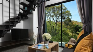 A modern living room with a wooden coffee table, a flat-screen TV, and a view of greenery through large windows. - Utopia Naiharn (Rawai)