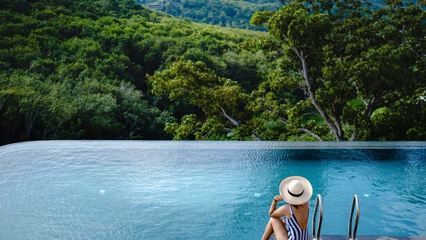 A person sitting by a pool with a view of a forested hillside. - Utopia Naiharn (Rawai)