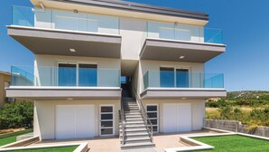 Un immeuble résidentiel moderne à plusieurs étages, doté de balcons en verre, d’un escalier central et d’une pelouse bien entretenue.