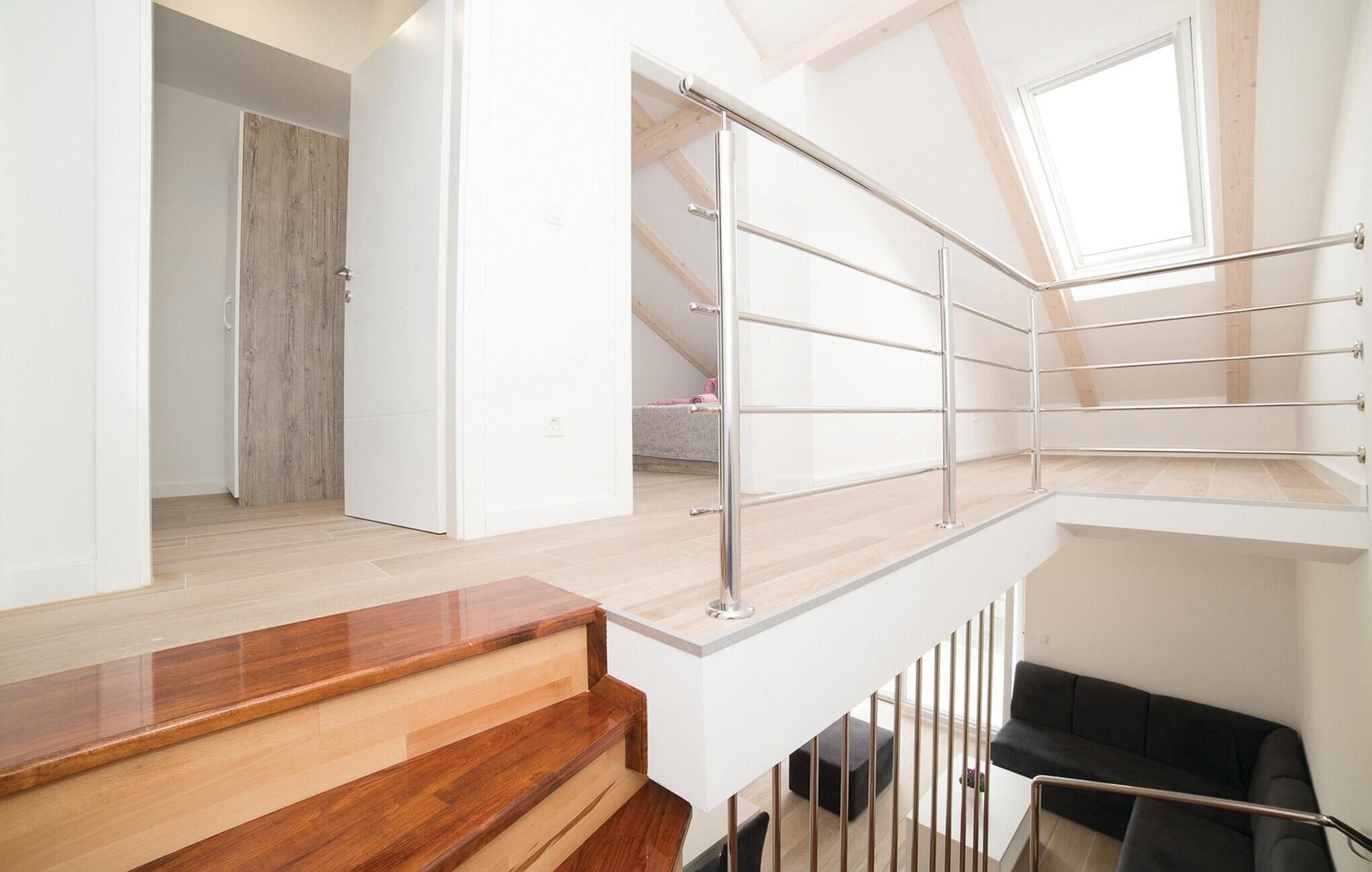 Um interior moderno com escada de madeira para um mezanino, um sofá preto e vista para um quarto com porta de madeira.