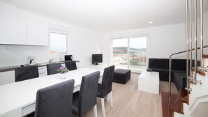 Une cuisine moderne avec des meubles blancs, un coin repas comprenant une table blanche et des chaises noires, et une grande fenêtre offrant une vue sur la ville.