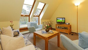 A cozy living room with a sofa, armchairs, a wooden coffee table, a TV, and a lamp. - Vacation apartment forest and sea (Loddin)