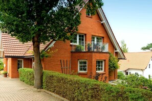 A two-story brick house with a sloped roof, a balcony on the second floor, and a paved driveway.