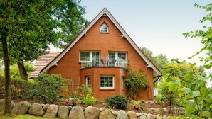 A two-story brick house with a balcony, surrounded by a stone wall and greenery. - Vacation apartment forest and sea (Loddin)