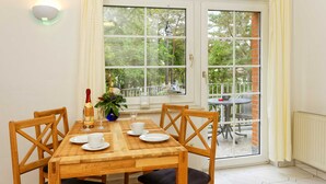 A dining area with a wooden table and chairs, a potted plant, and a view of the outdoors through large windows. - Vacation apartment forest and sea (Loddin)