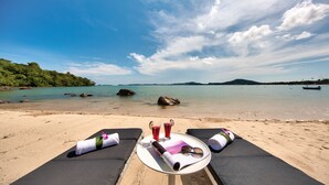 A beachside view with a table set for two, featuring sun loungers, a plate, glasses, and a bottle. - Baan Benjamart (Koh Samui)