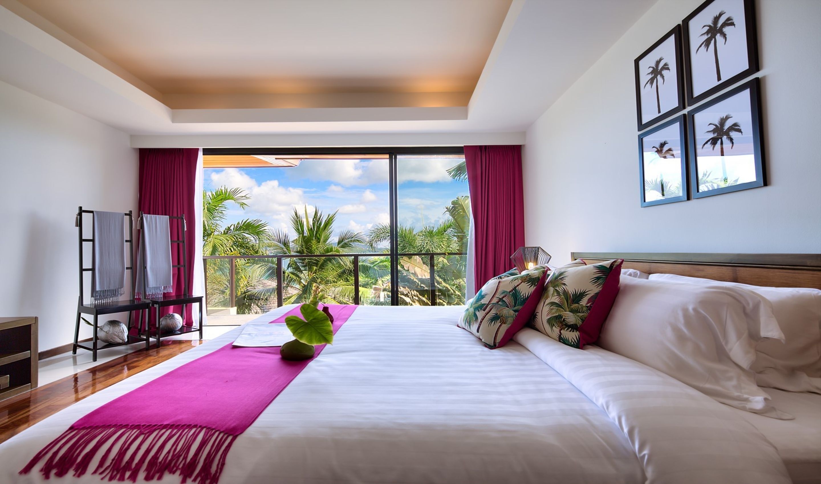 A hotel room with a large bed, a balcony with a view of palm trees, and a ceiling with recessed lighting.