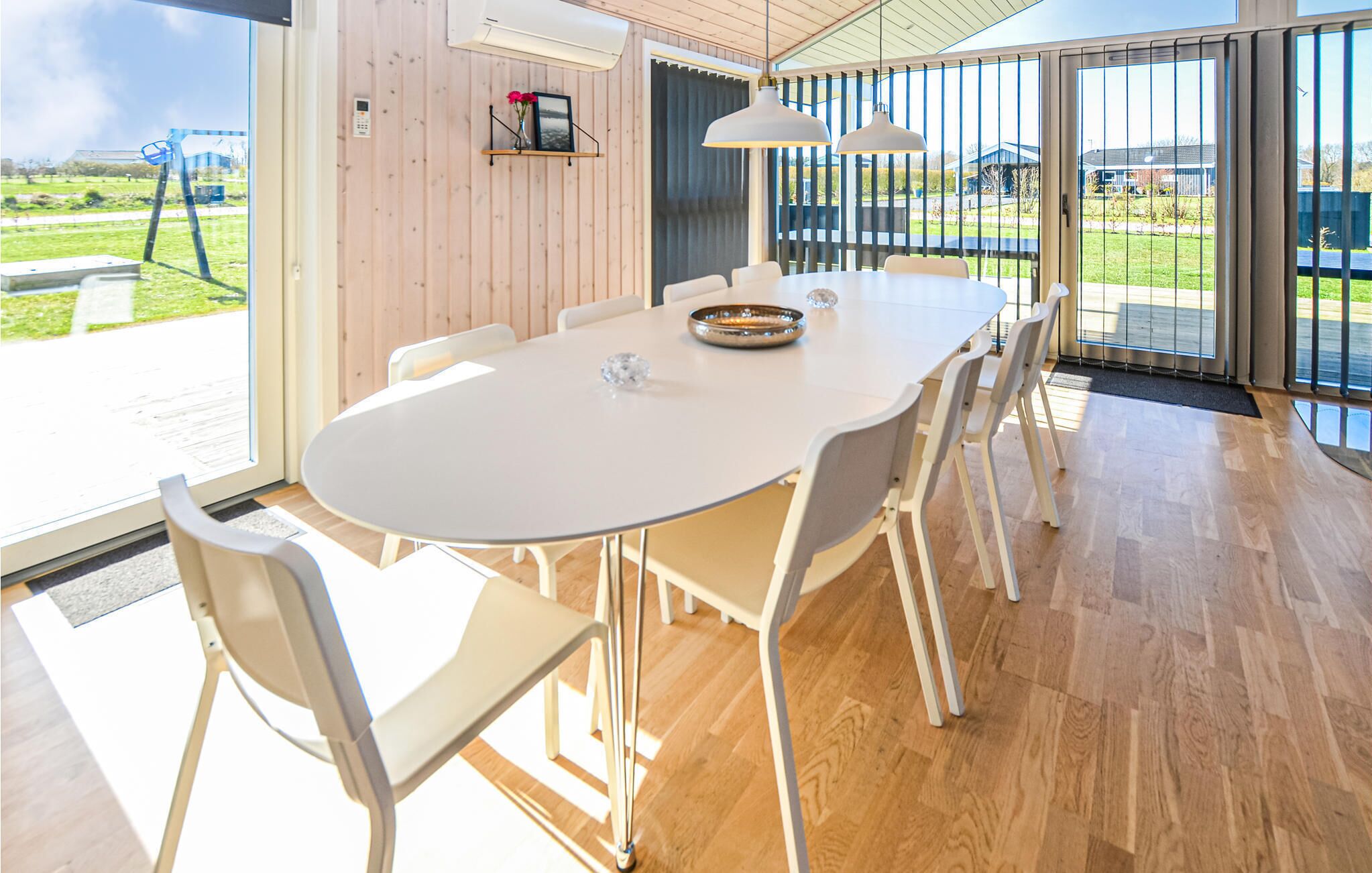 A modern dining area with a white table and chairs, large windows, and a view of the outdoors.