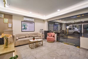 Eine moderne Lobby mit einem beigefarbenen Sofa, einem pinken Sessel, einem Couchtisch und einer gerahmten Illustration eines Baumes an der Wand.