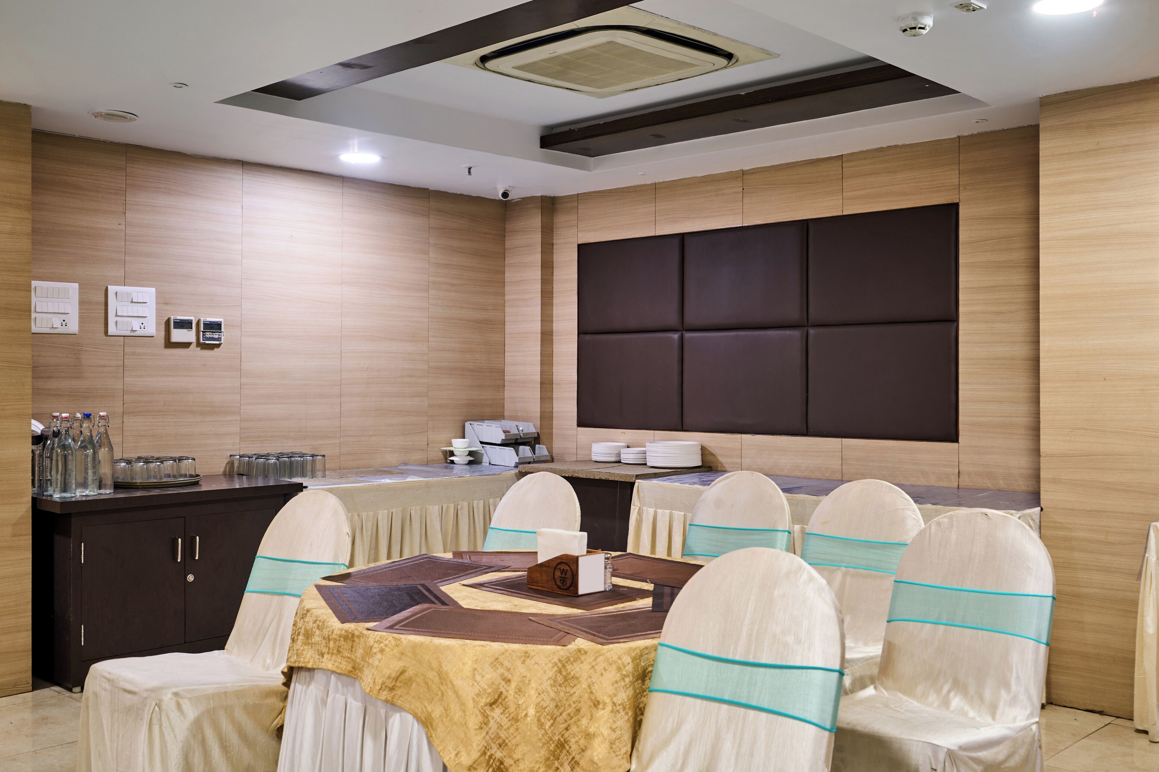 A conference room with a round table, chairs, a dark padded headboard, and a wooden wall.