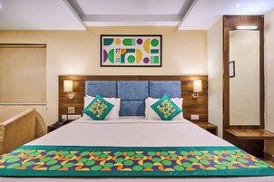Hotelkamer met een bed, hoofdeinde, twee wandlampen, nachtkastje, stoel en een abstract kunstwerk in een lijst aan de muur.