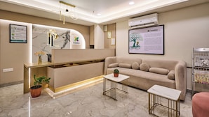 A reception area with a marble floor, a reception desk, a sofa, a small table, and a plant. - Treebo Premium PL Grand, Visakhapatnam (Visakhapatnam)