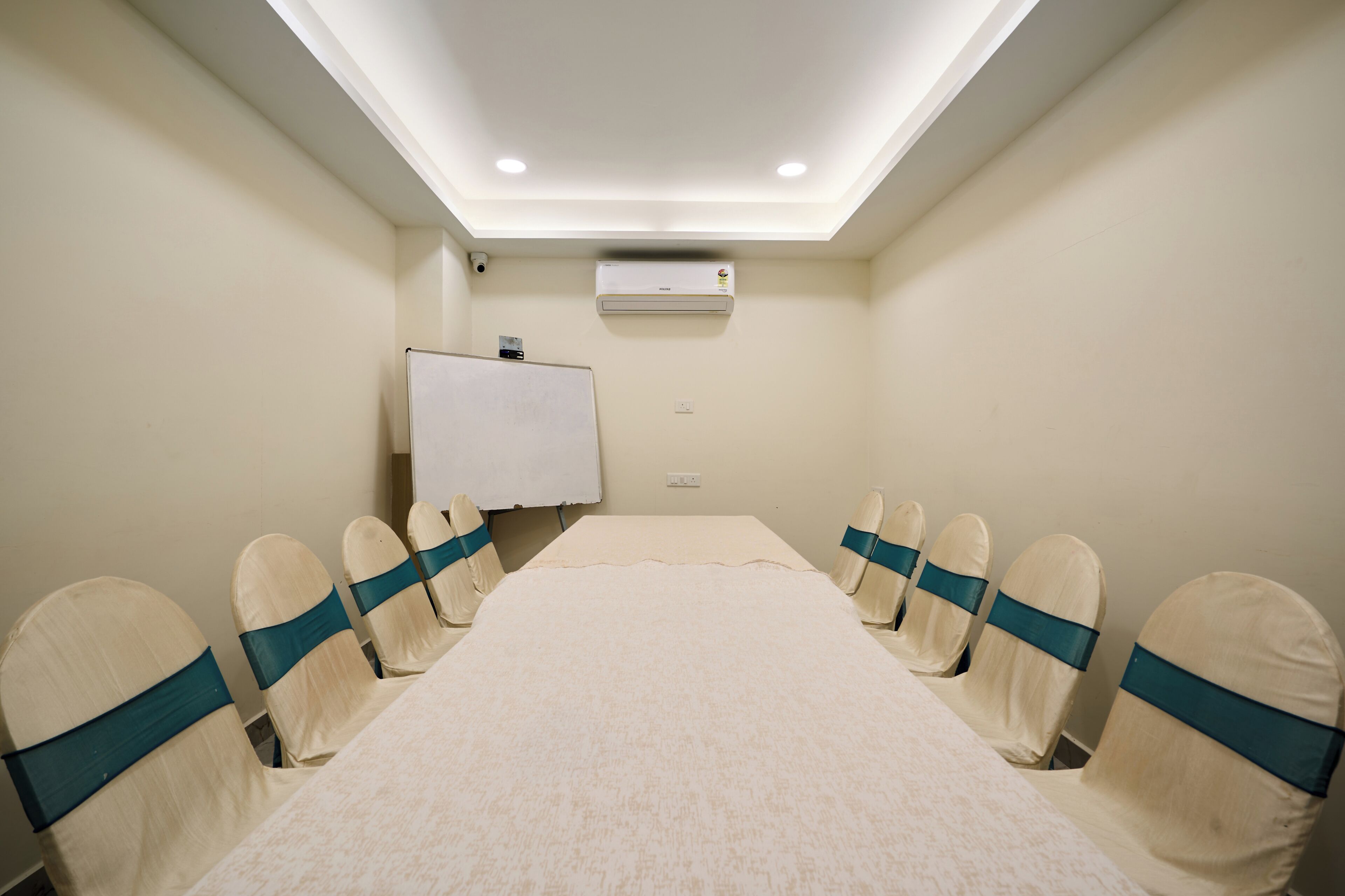 A conference room with a long table, chairs with teal sashes, an air conditioning unit, and a whiteboard.